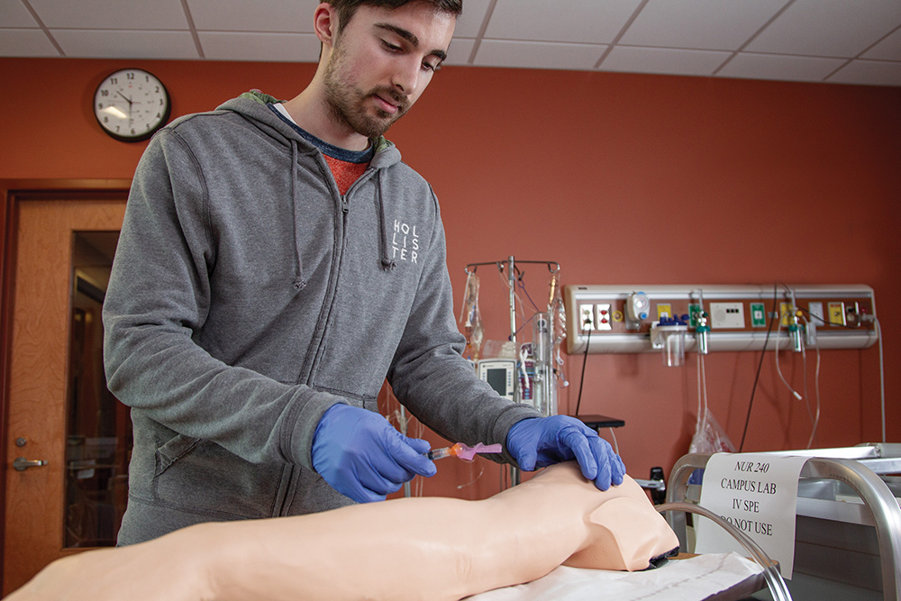 a student administers an IV to a dummy in a medical lab setting